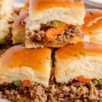 Philly cheesesteak sliders stacked on a parchment covered wooden cutting board.
