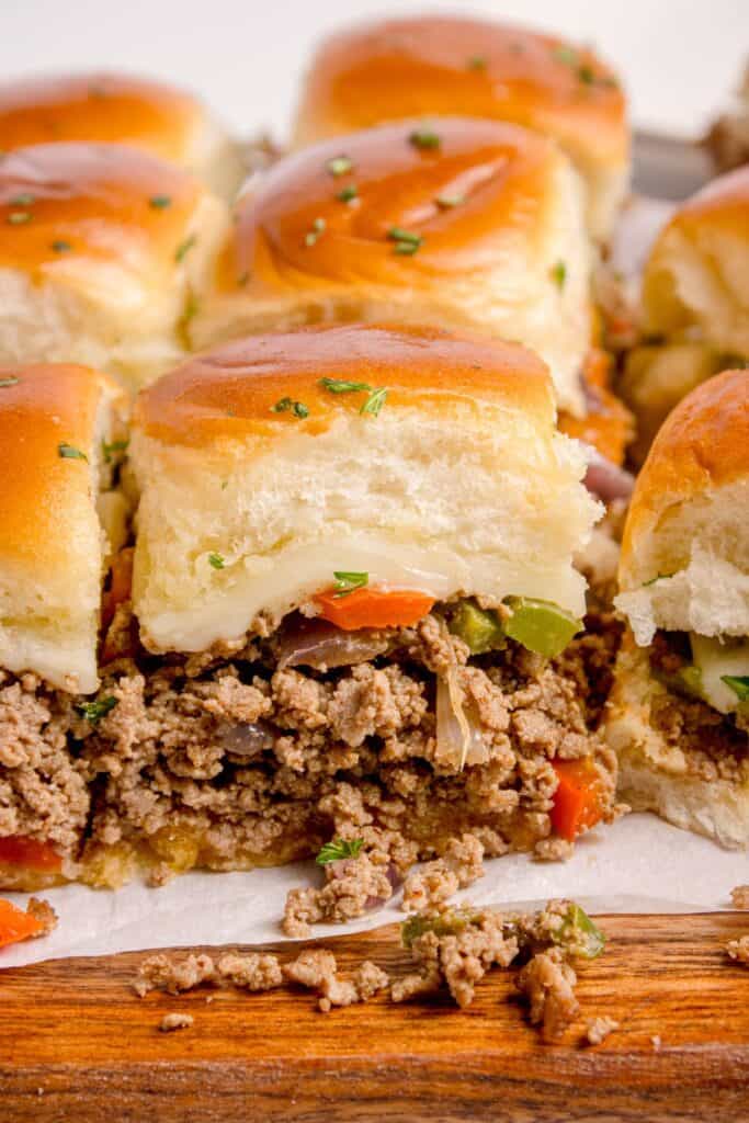 Philly cheesesteak sliders sliced on a parchment covered wooden cutting board.