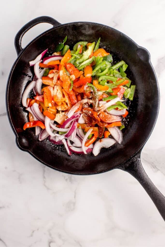 Raw peppers and onions in a cast iron pan.