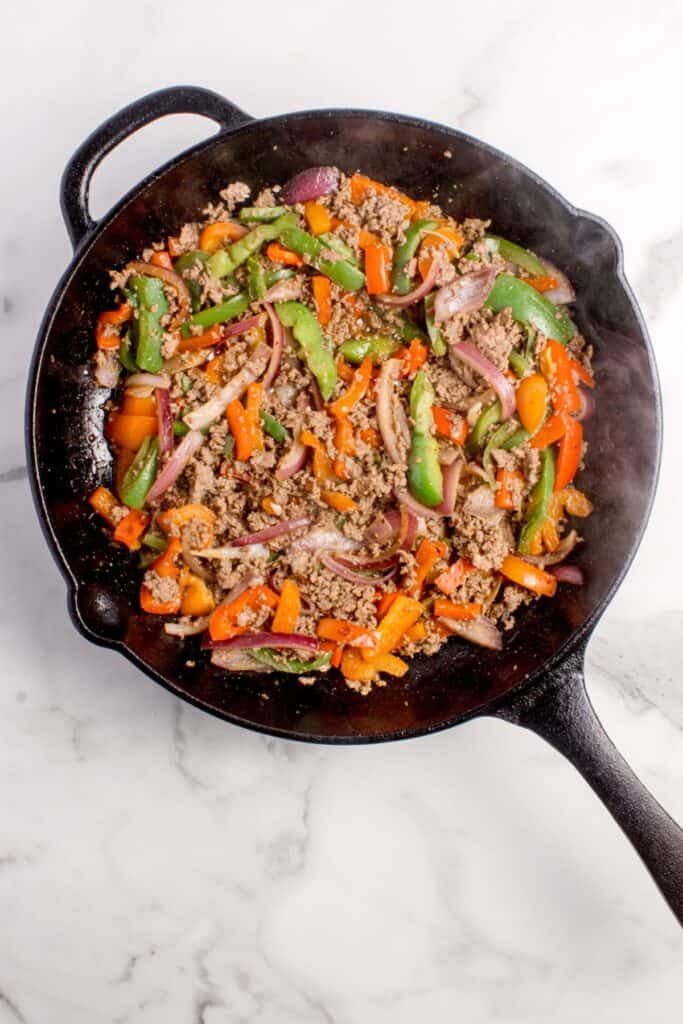 Cast iron pan with cooked peppers, onion, and beef.