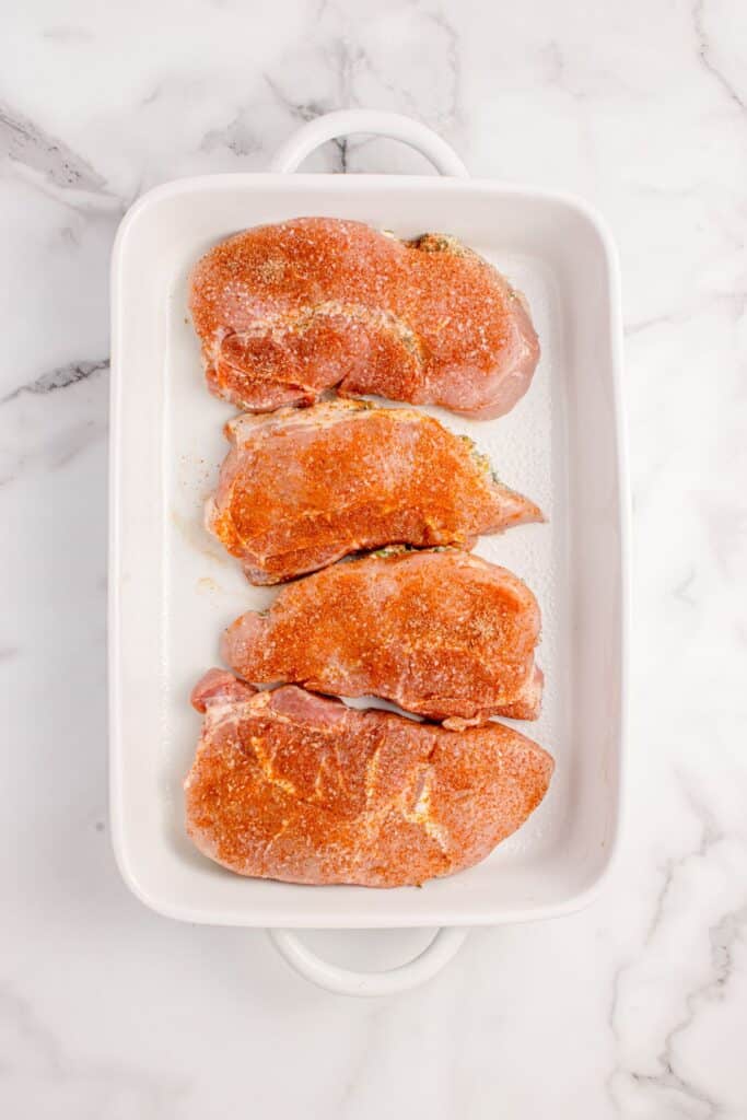 Raw pork chops in a white baking dish.