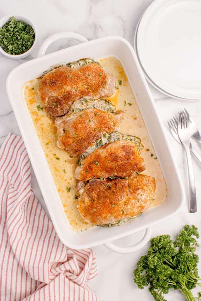 Four stuffed pork chops in a white baking dish.