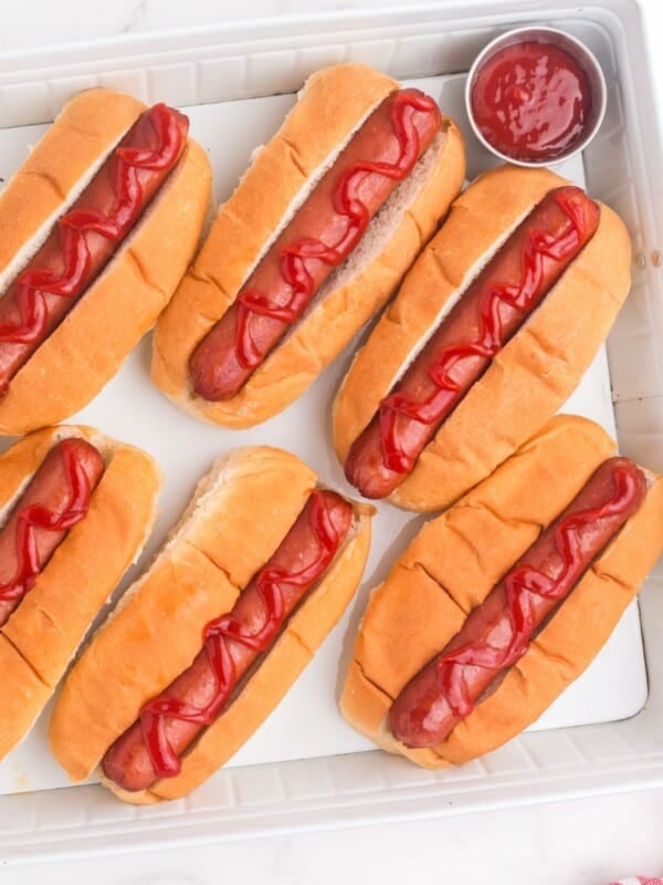 Several completed hot dogs on a tray with a little cup of ketchup.