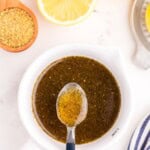 Lemon pepper sauce in a small white bowl with a metal spoon lifting a small amount above the bowl.