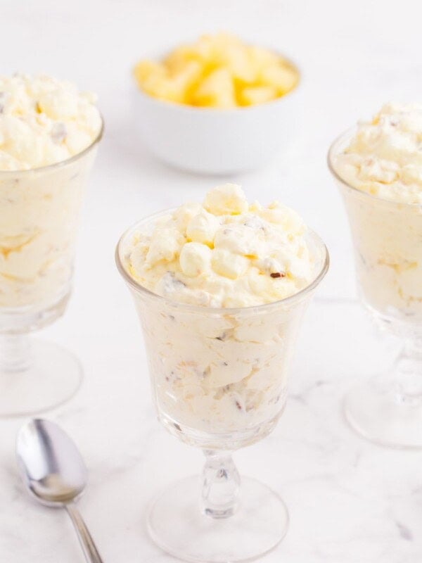 Three glasses of pineapple fluff, a spoon, and a bowl of pineapple.
