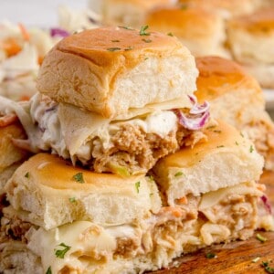 Chicken sliders stacked in a pyramid on a wooden cutting board.