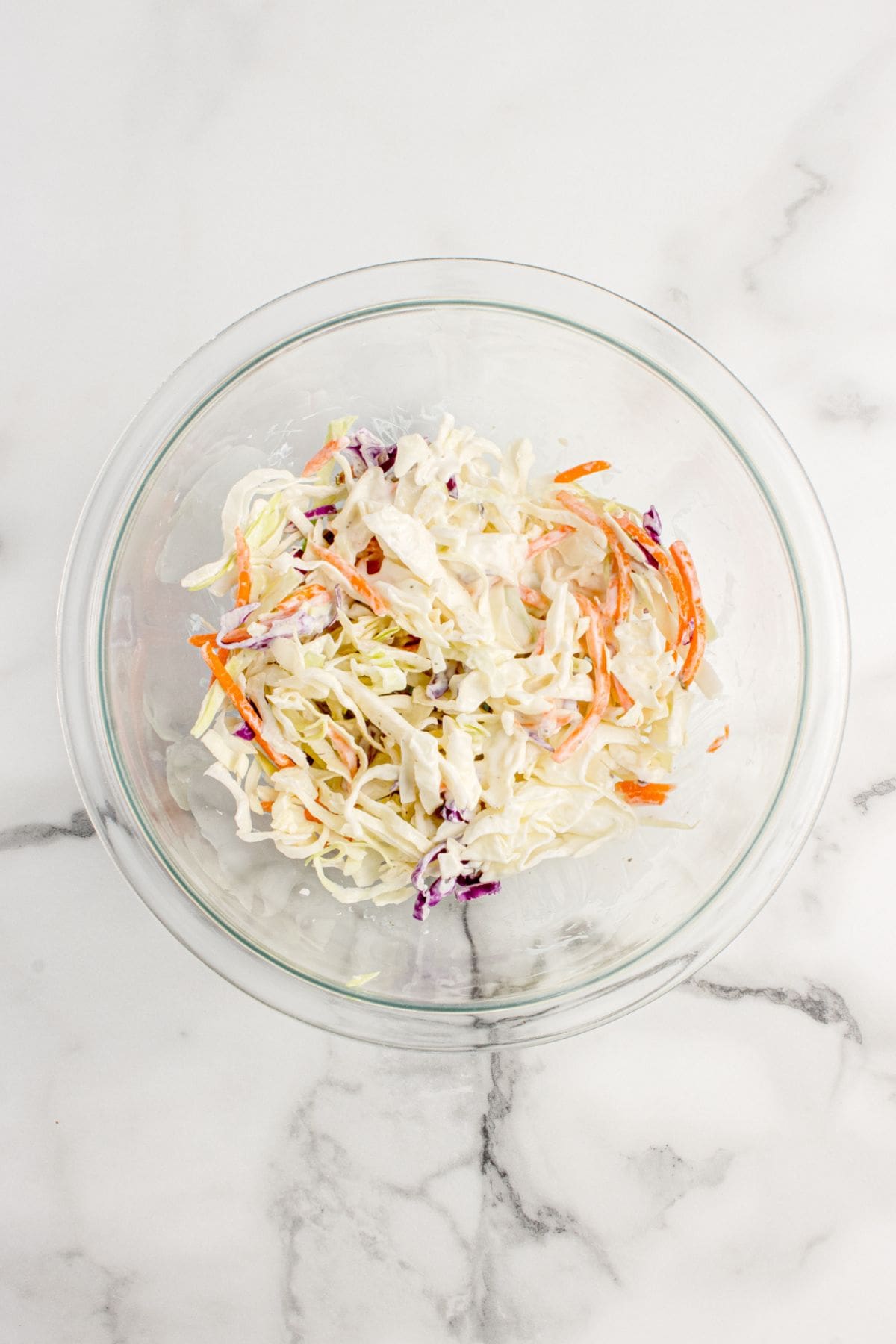 Glass mixing bowl with coleslaw mix and ranch dressing tossed together.