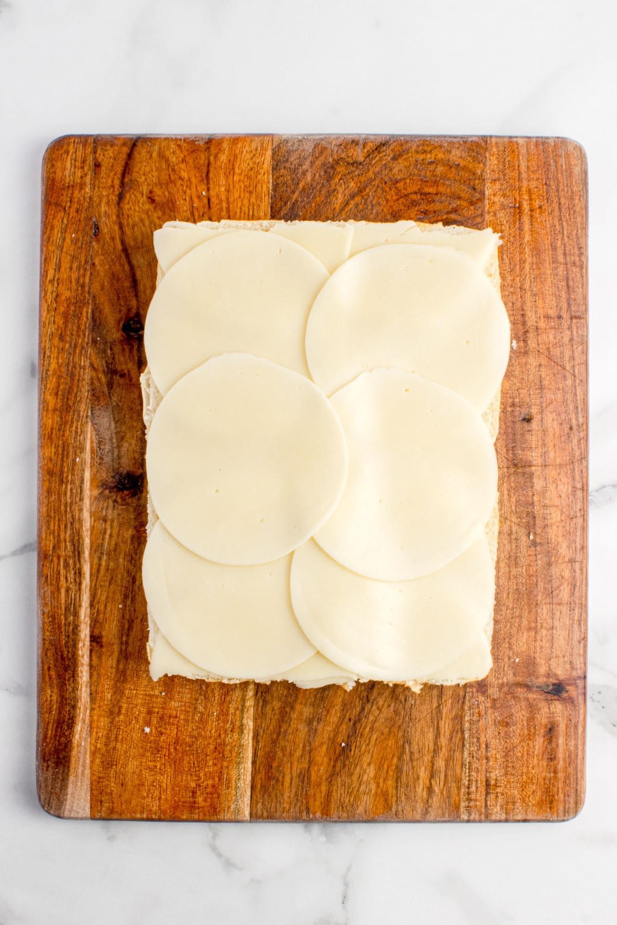 A layer of sliced provolone cheese lines the bottom half of the Hawaiian rolls.