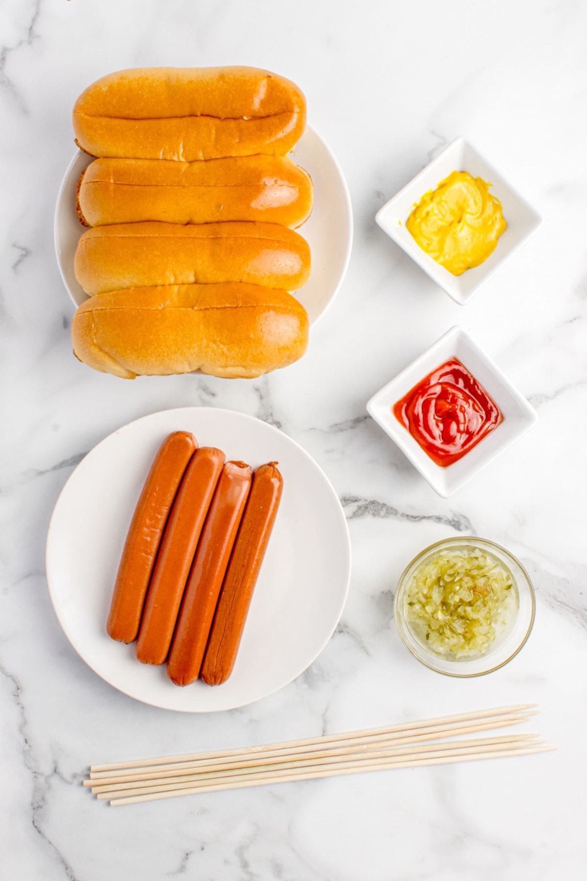 Ingredients for grilled hot dogs: hot dogs, buns, wooden skewers, ketchup, mustard, and relish.
