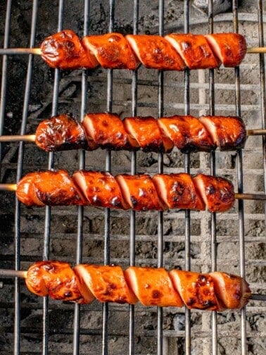 Hot dog cooking on a charcoal grill.
