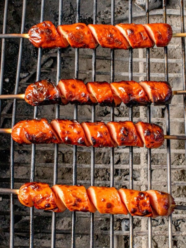 Hot dog cooking on a charcoal grill.