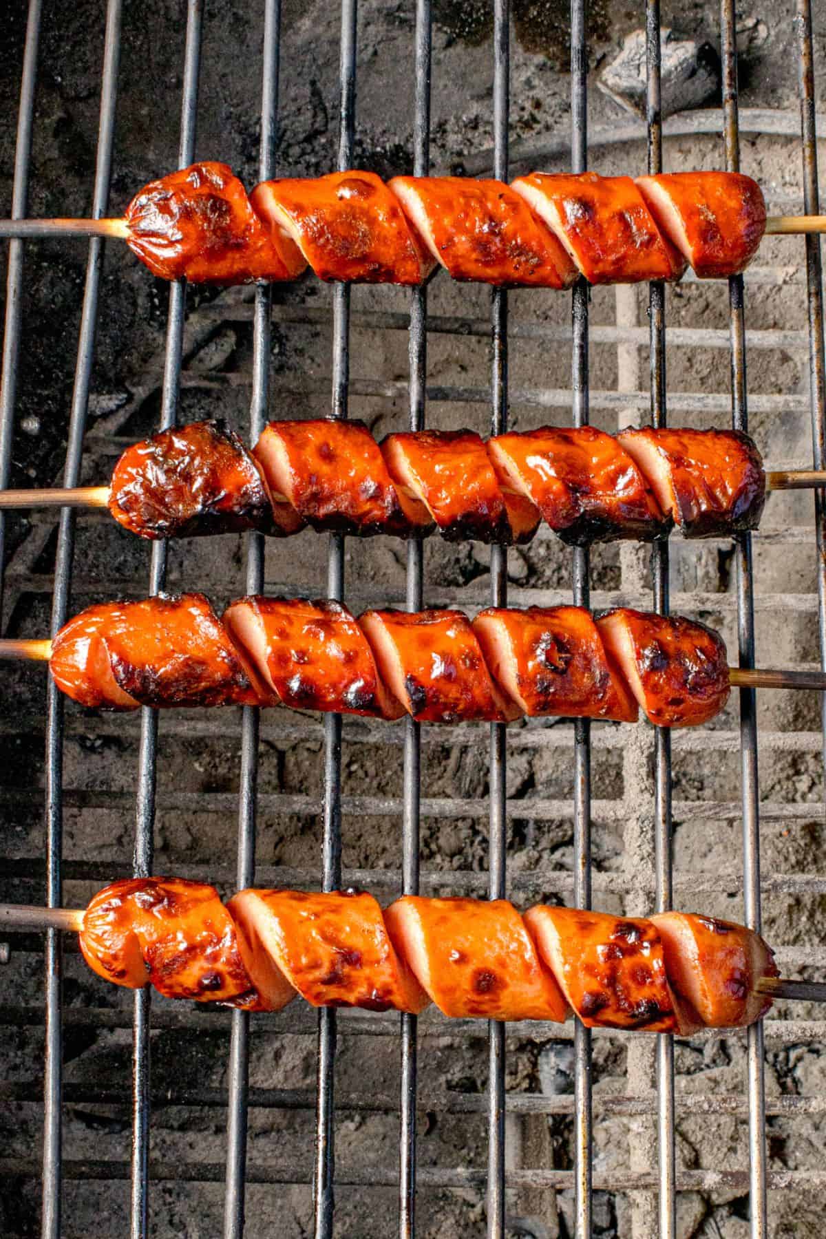 Hot dog cooking on a charcoal grill.