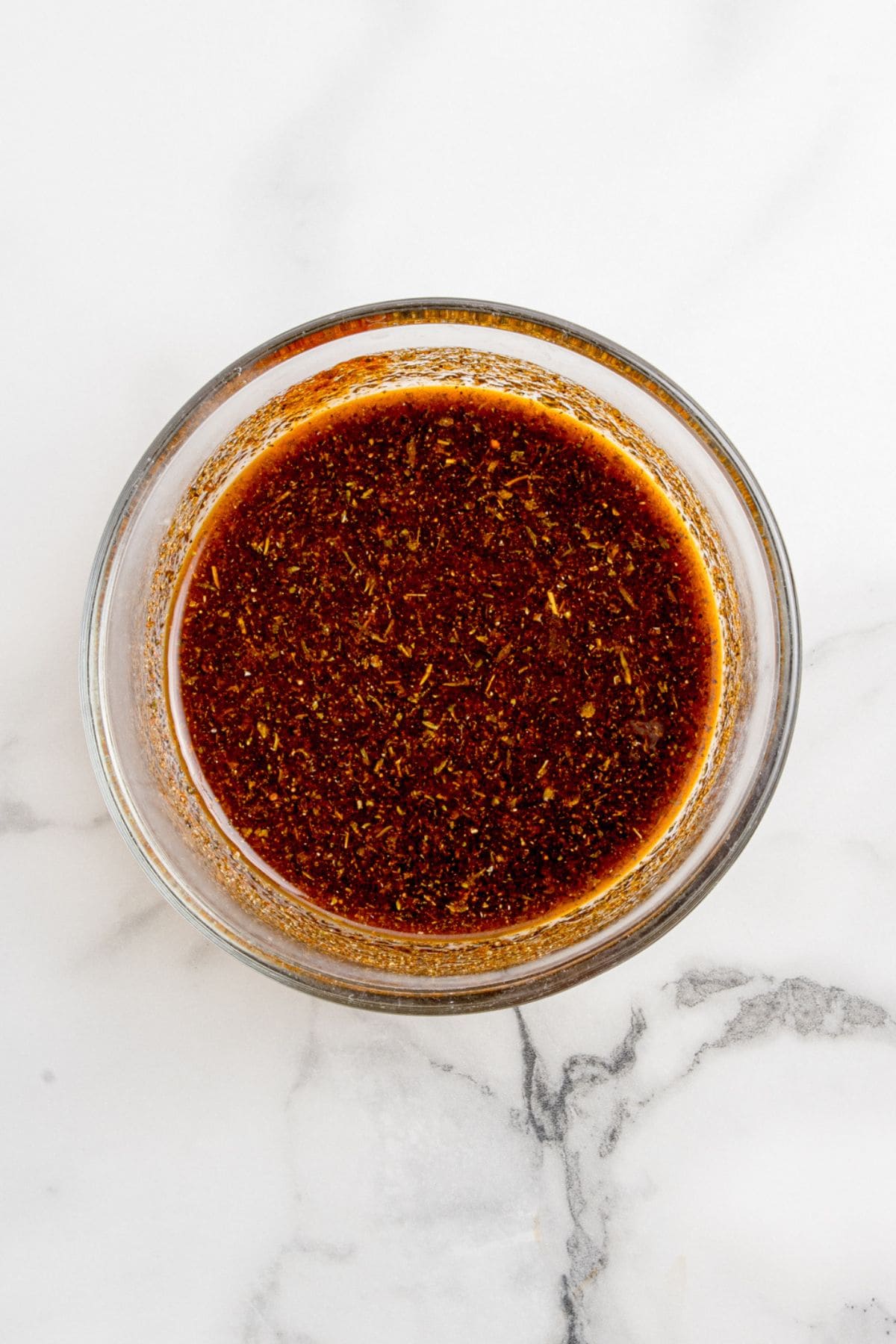 A glass mixing bowl with oil and spices to create a marinade.