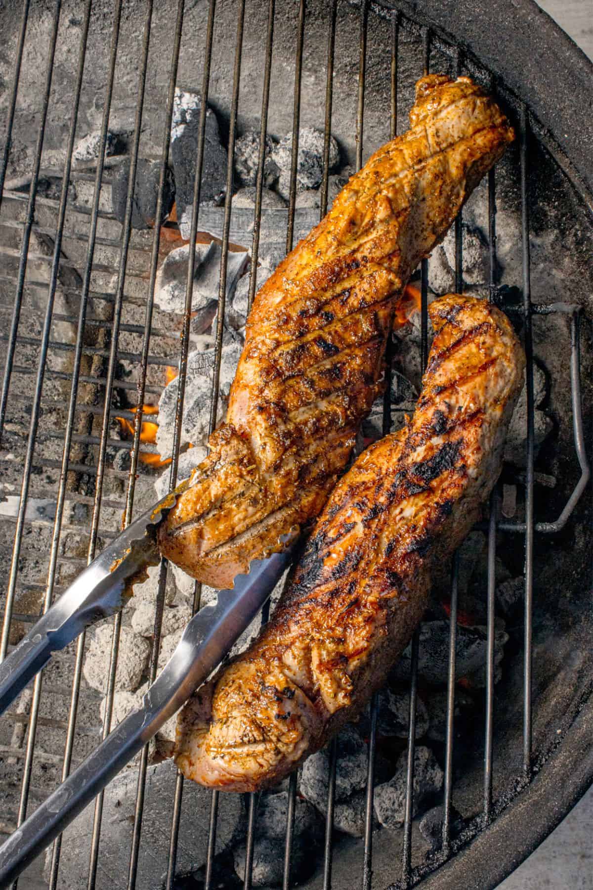 Pork tenderloins cooking on a charcoal grill.