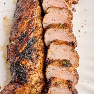 Grilled pork tenderloin with one piece uncut and the other cut into medallions on a white serving platter.