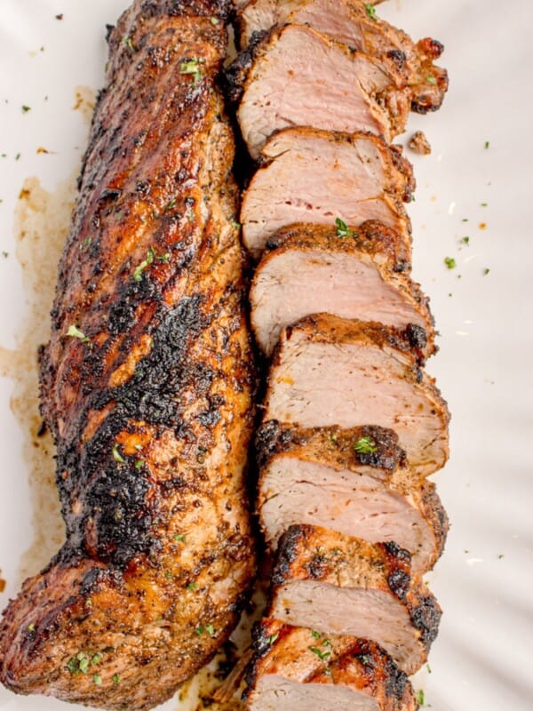 Grilled pork tenderloin with one piece uncut and the other cut into medallions on a white serving platter.