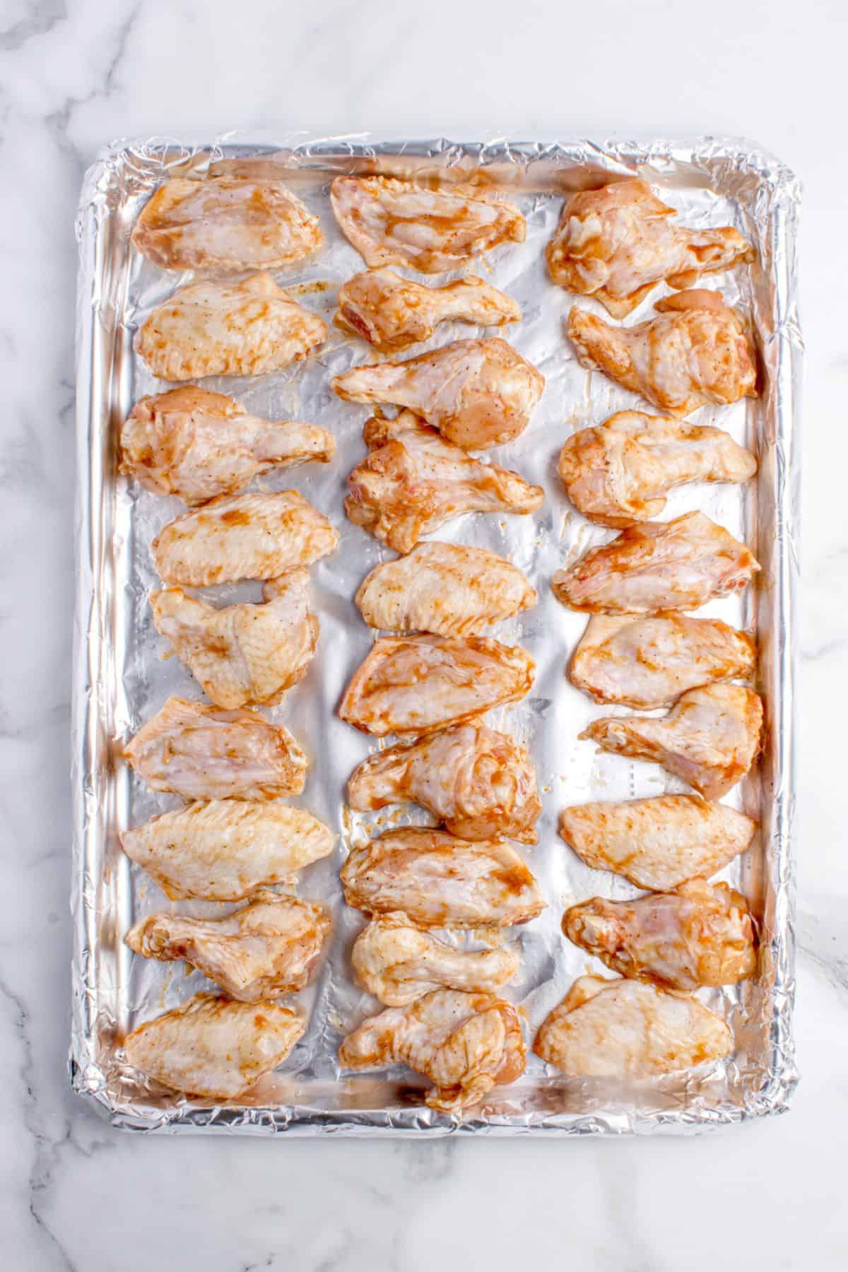 Marinated and refrigerated chicken wings on a foil lined baking sheet.