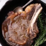 Completed ribeye steak in a cast iron pan with a sprig of rosemary.