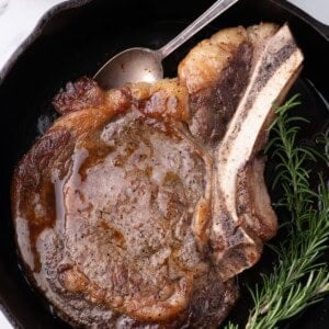 Completed ribeye steak in a cast iron pan with a sprig of rosemary.