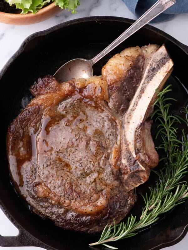 Completed ribeye steak in a cast iron pan with a sprig of rosemary.