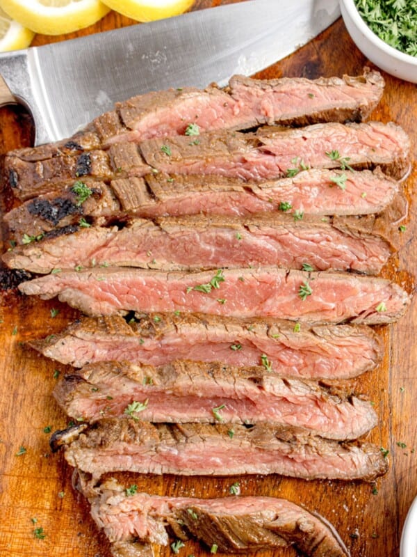 Cooked and sliced flank steak on a wooden cutting board.