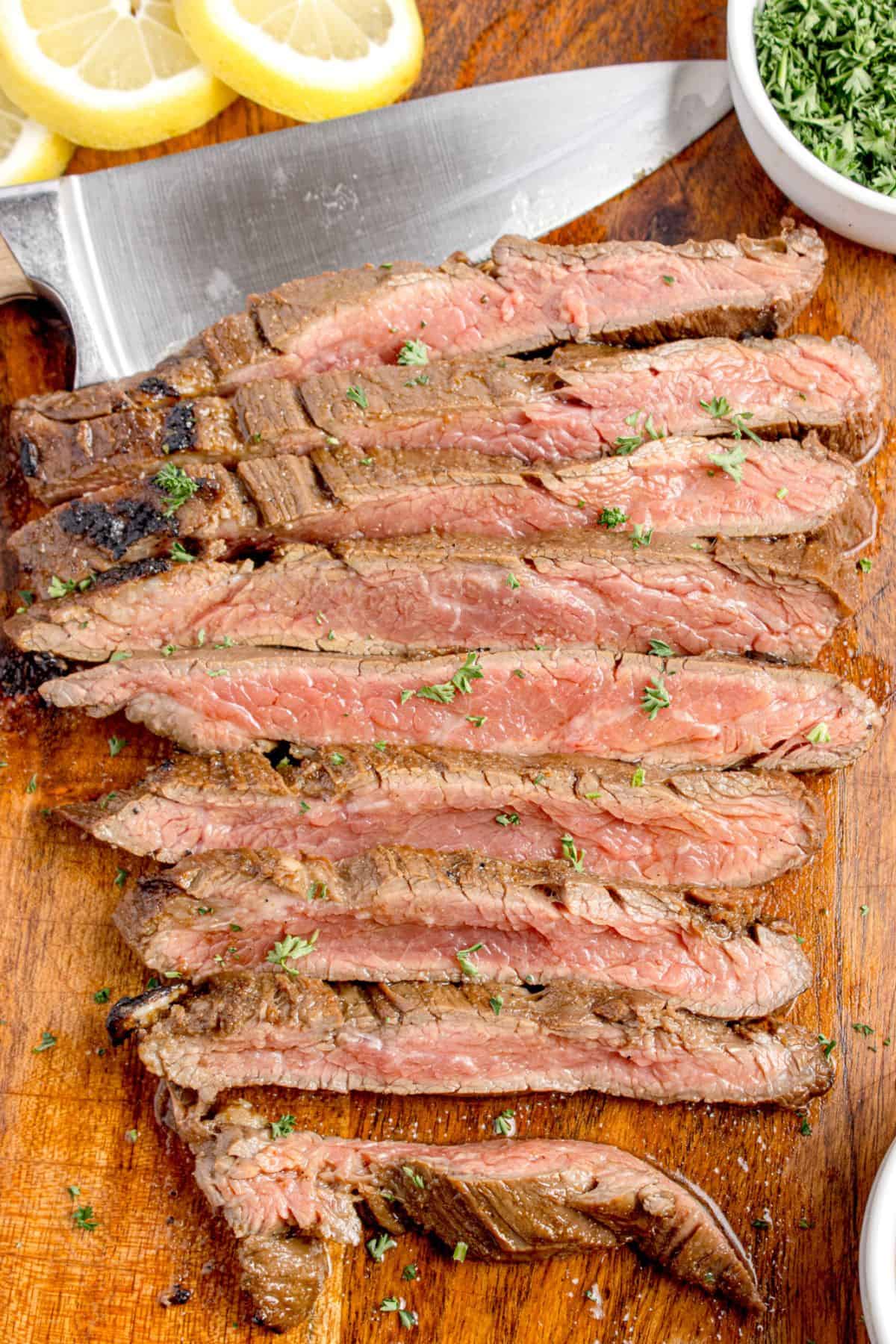 Cooked and sliced flank steak on a wooden cutting board.