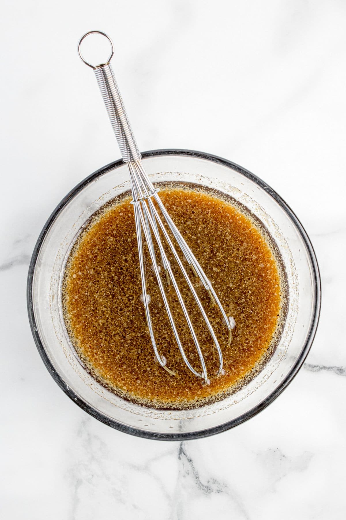 Flank steak marinade in a glass mixing bowl with a wire whisk.