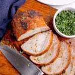 Grilled pork loin sliced on a wooden cutting board. Slices are fanned out to show interior texture.