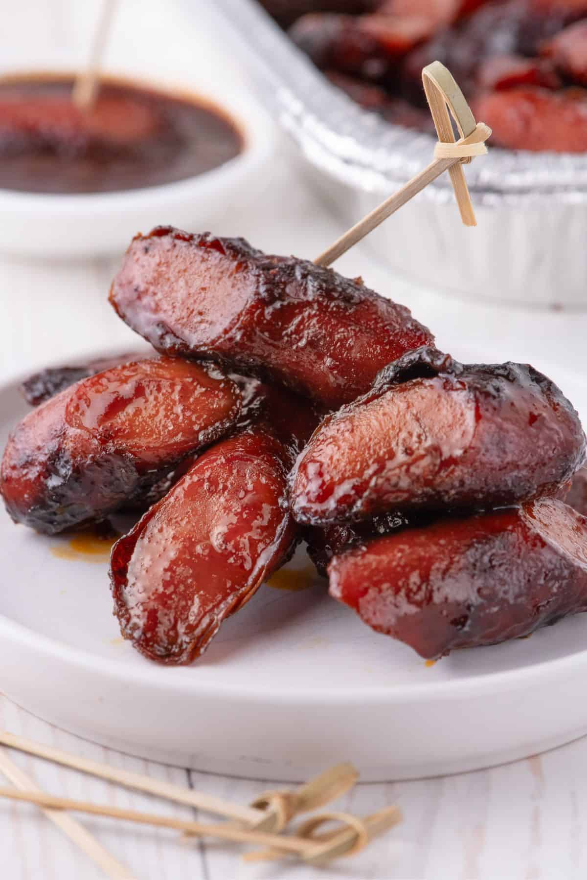 A serving of hot dog burnt ends piled up on a white plate. One hot dog has a toothpick in the top.
