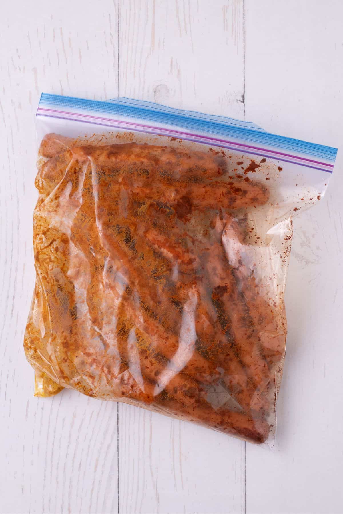 Hot dogs marinating in a plastic zip top bag with mustard and smoked paprika.