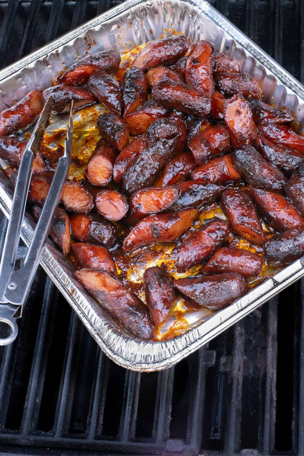 Hot dog burnt ends in a foil tray on grill grates.