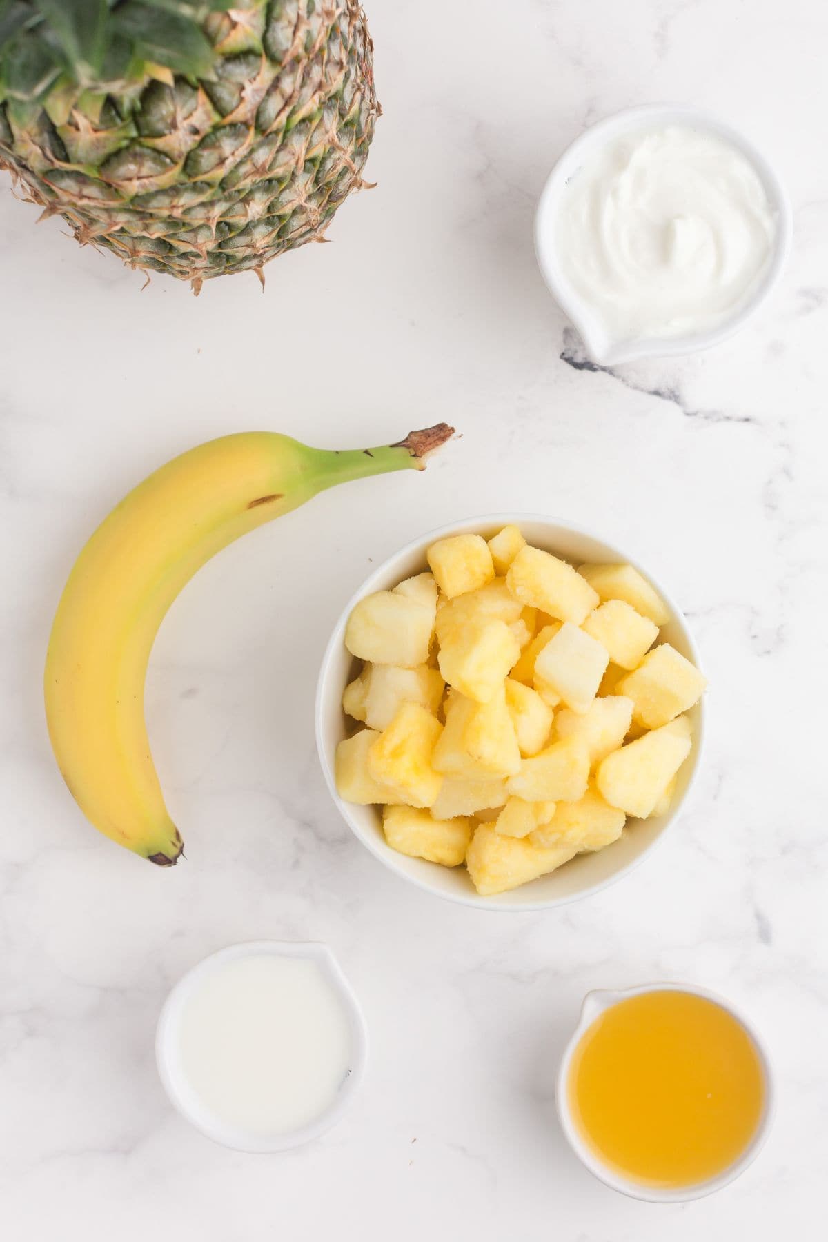 Ingredients for pineapple smoothie: Vanilla greek yogurt, banana, pineapple, milk, and pineapple juice.