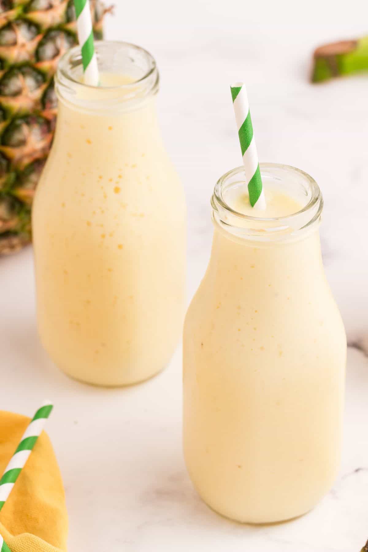Pineapple smoothies in milk style glasses. Each glass has a white and green striped straw.