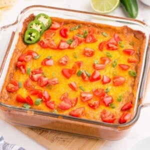 Completed refried bean dip in a glass baking pan. Dip has been garnished with diced tomatoes, green onions, and sliced jalapenos.