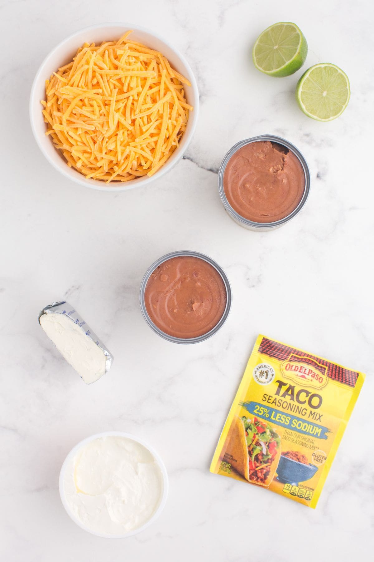 Ingredients for refried bean dip: cheddar cheese, lime juice, refried beans, cream cheese, sour cream, and taco seasoning.