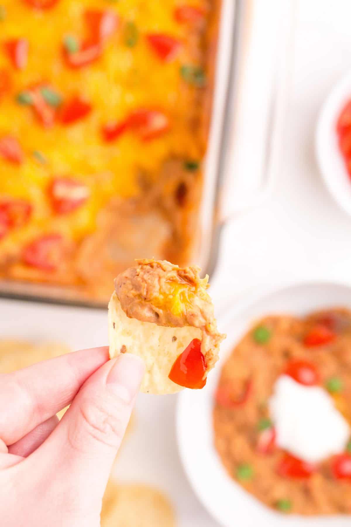 A hand holding a tortilla chip with refried bean dip on it.