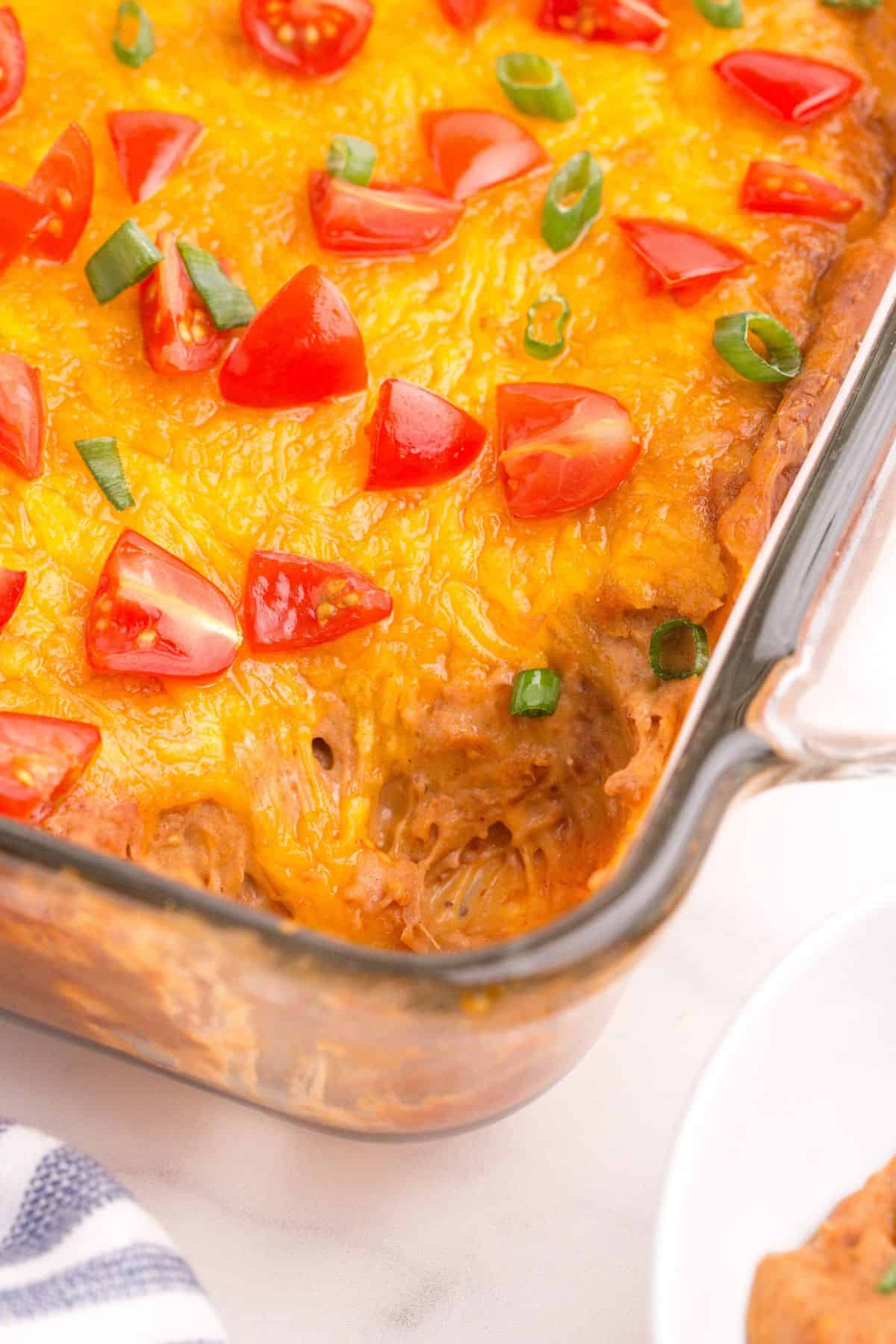A small serving of the completed refried bean dip has been scooped out of the glass baking dish.