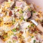 Loaded potato salad in a serving bowl with a spoon in it.