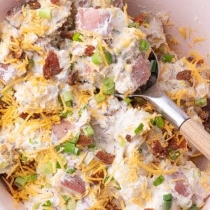 Loaded potato salad in a serving bowl with a spoon in it.
