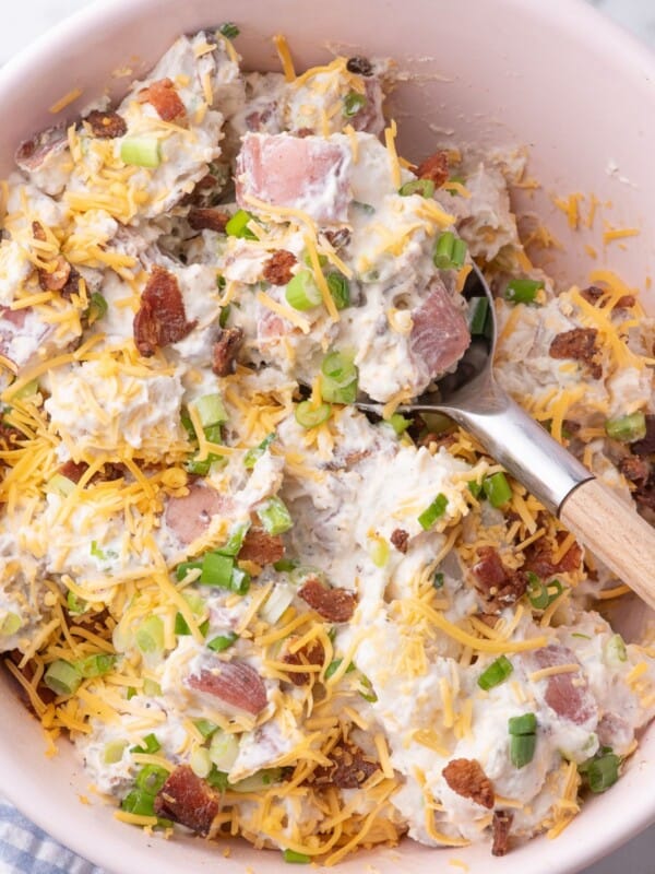Loaded potato salad in a serving bowl with a spoon in it.