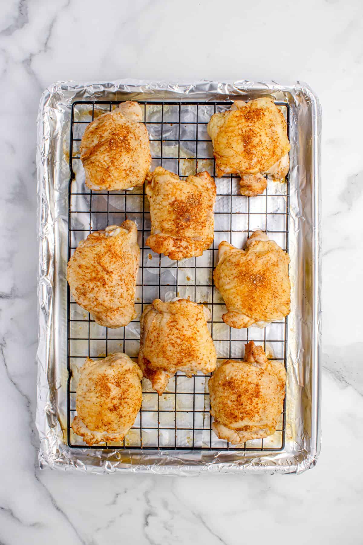 Chicken thighs partially baked on a aluminum foil lined baking sheet with a rack.