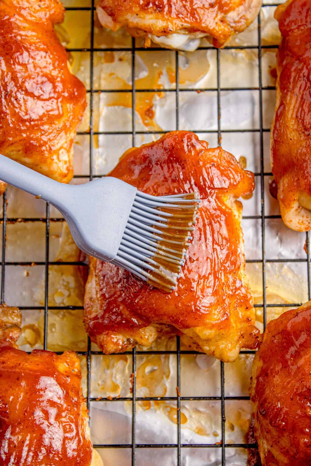 Chicken thigh is getting brushed with BBQ sauce.