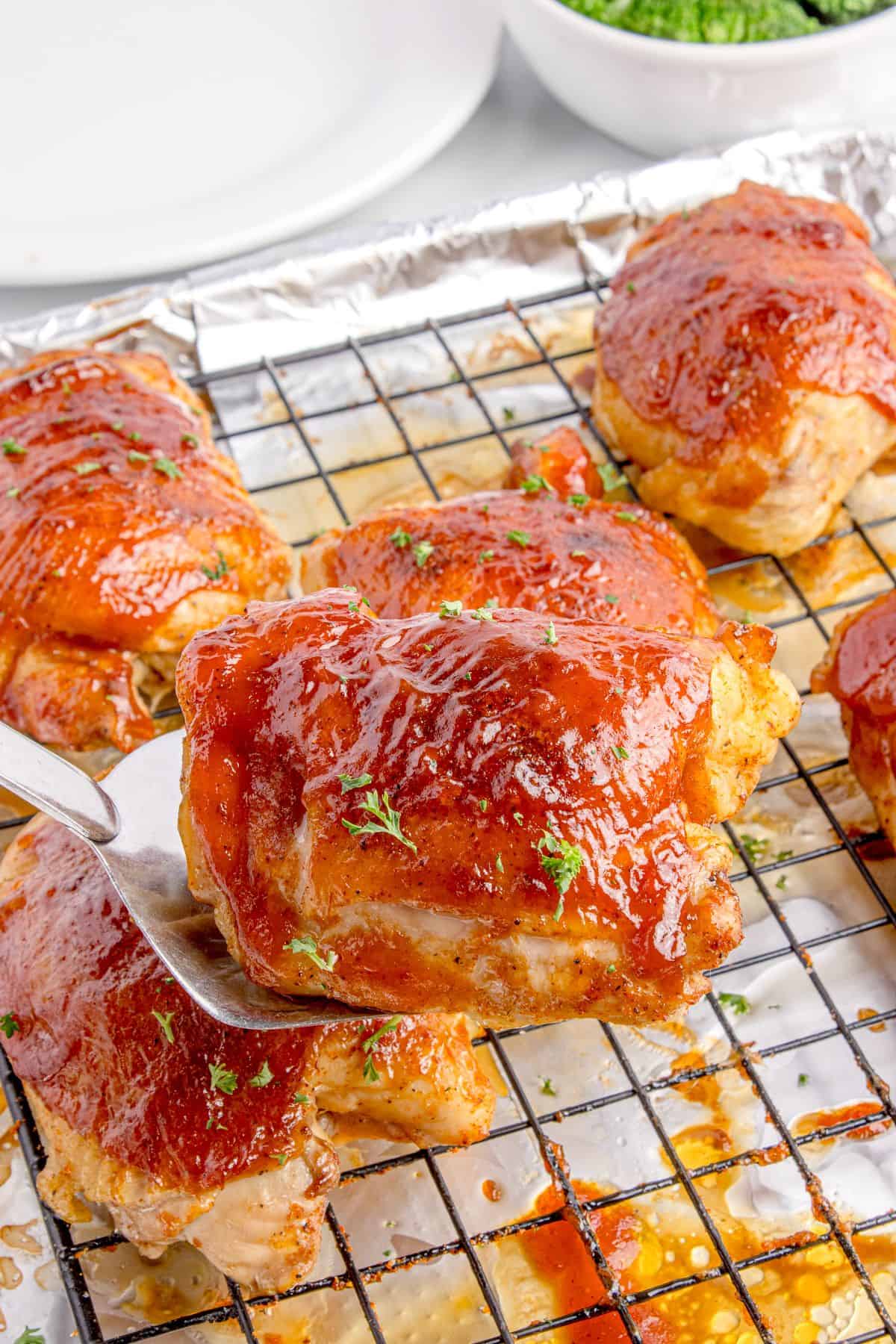 A completed chicken thigh is lifted with a spatula above the baking sheet.