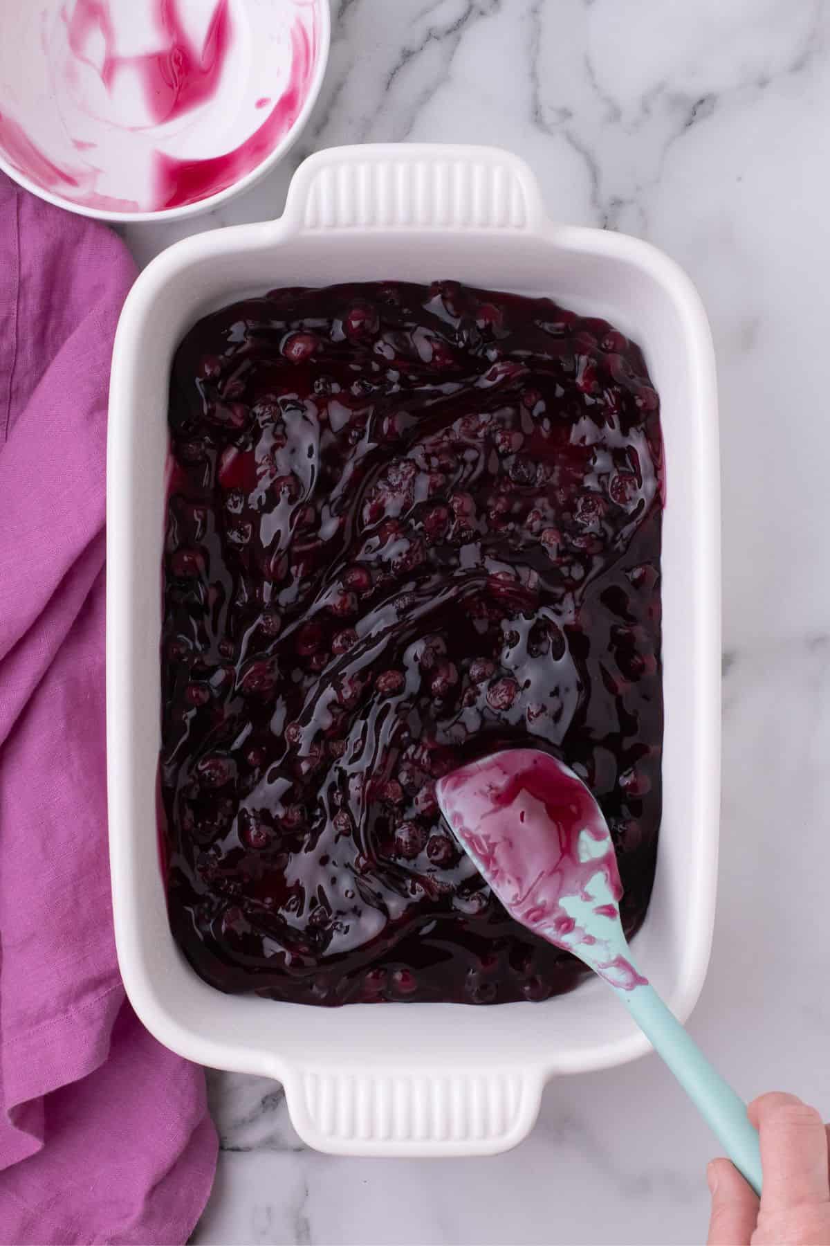 Blueberry pie filling is spread evenly at the bottom of a baking dish.