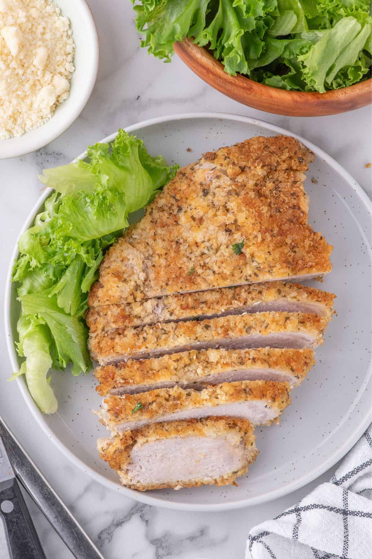 Parmesan crusted pork chop sliced on a white dinner plate.