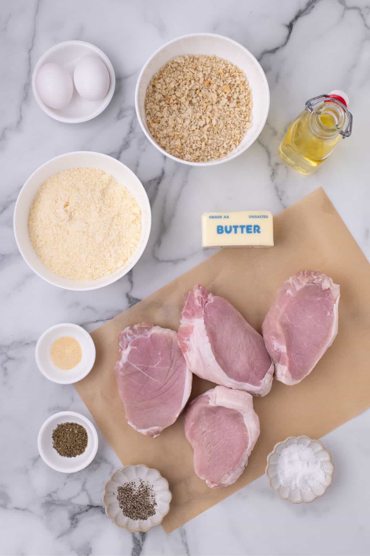 Ingredients for parmesan crusted pork chops: panko breadcrumbs, parmesan cheese, eggs, salt, black pepper, garlic powder, dried parsley, pork chops, olive oil, and butter.