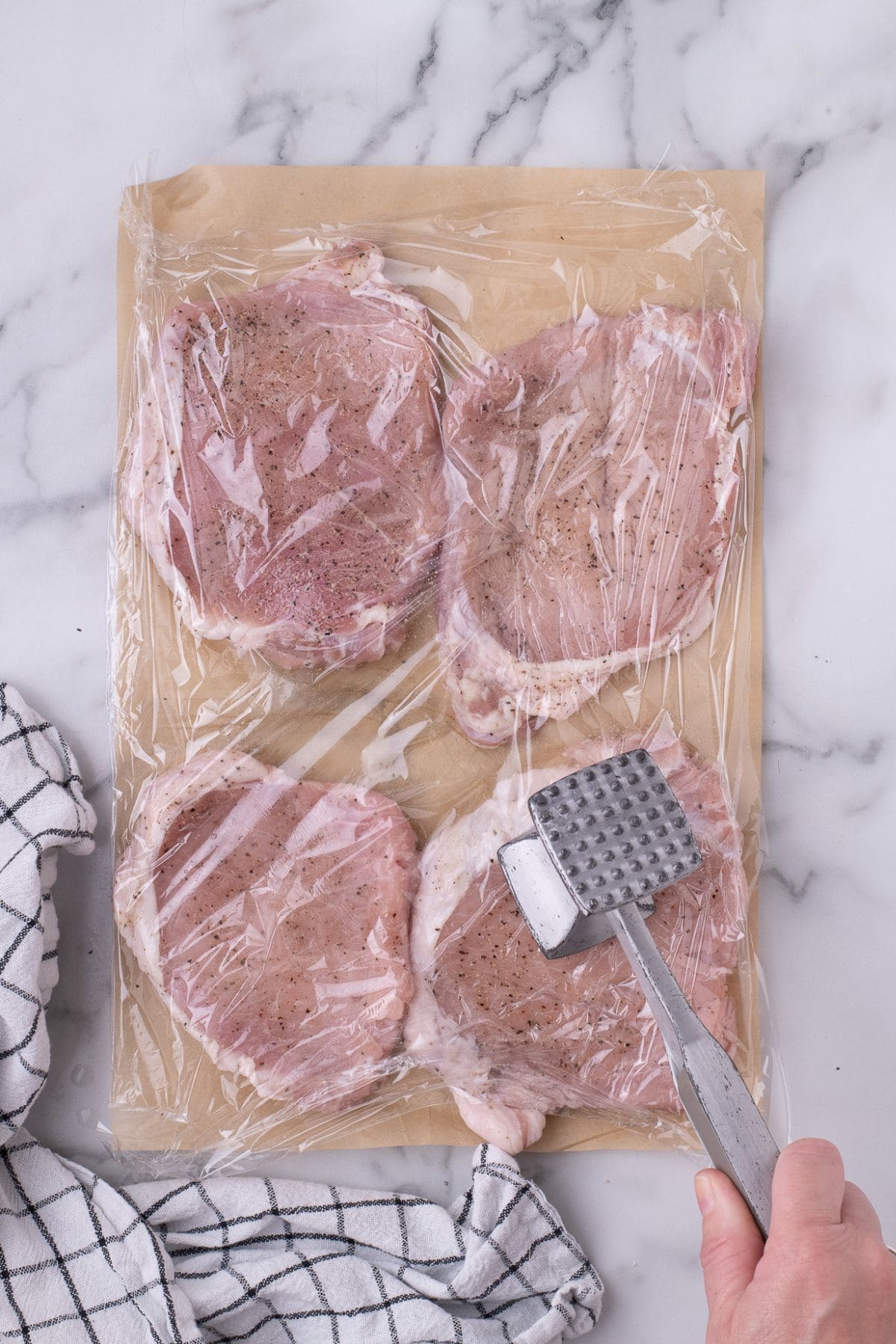 Pork chops being pounded with a kitchen mallet.