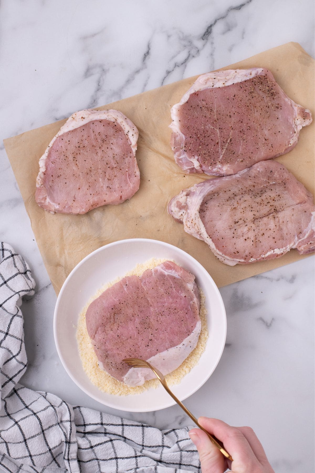Pork chop being coated in parmesan.