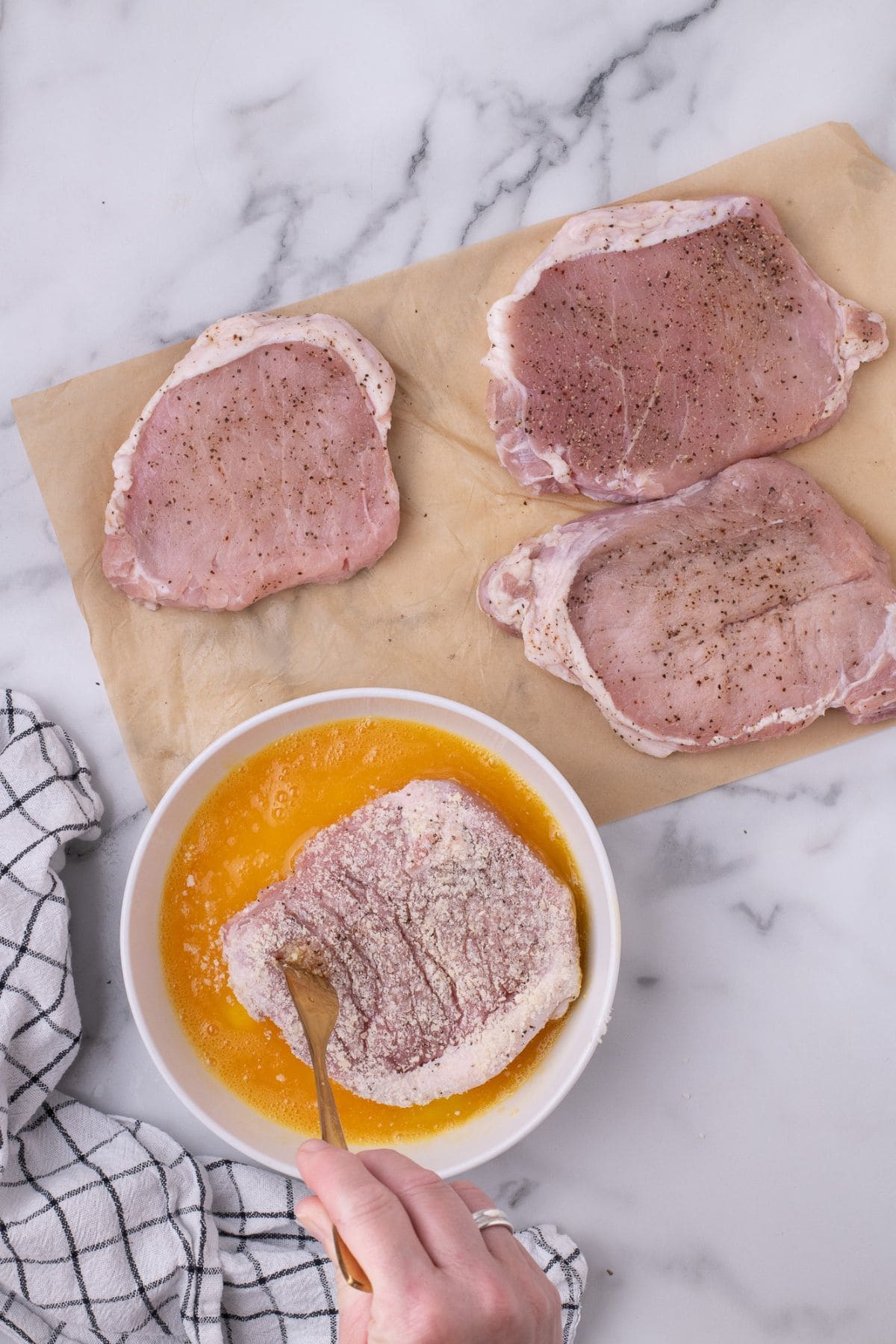 Pork chop being coated in egg.