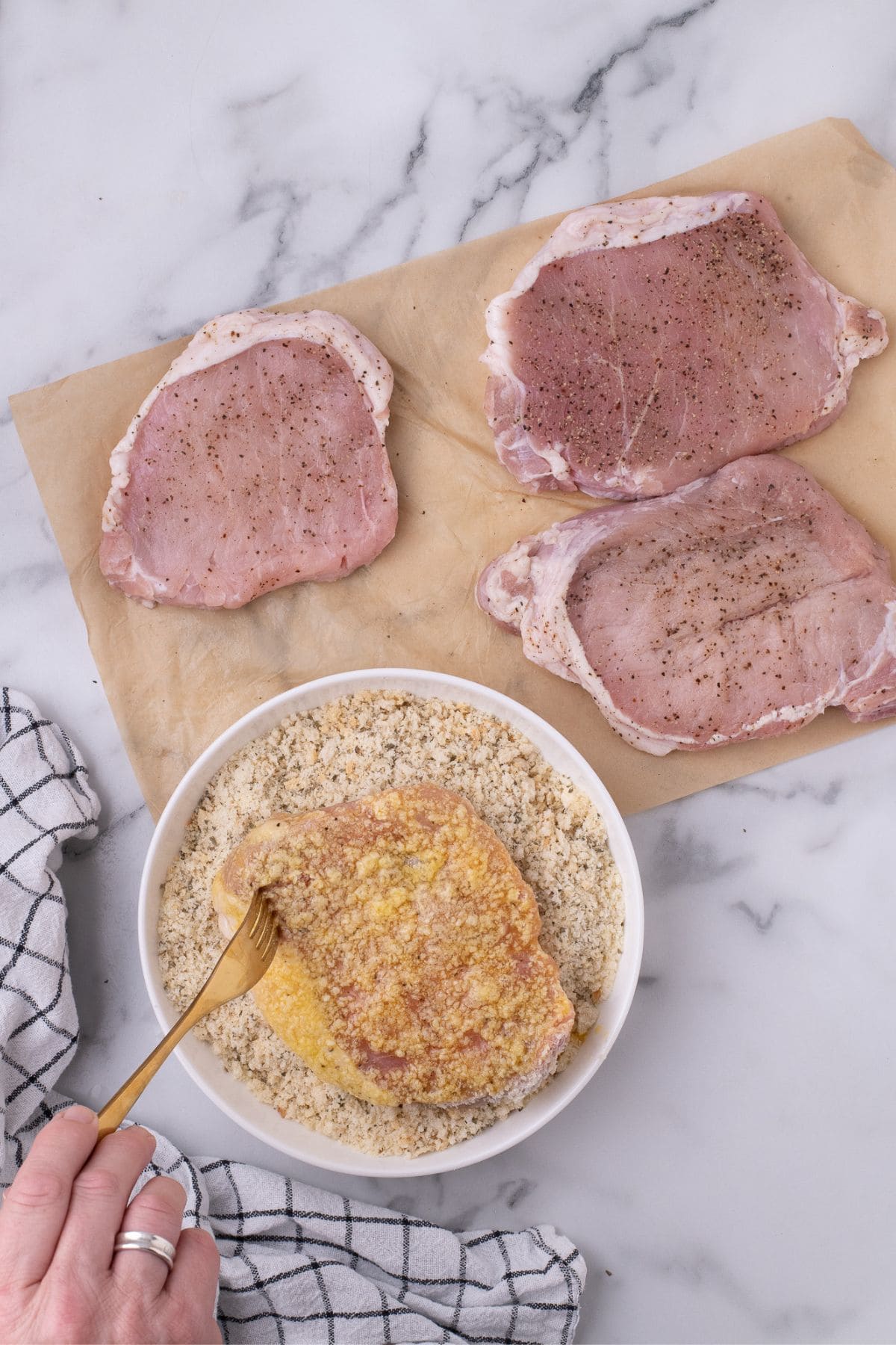 Raw pork chop being coated in panko.
